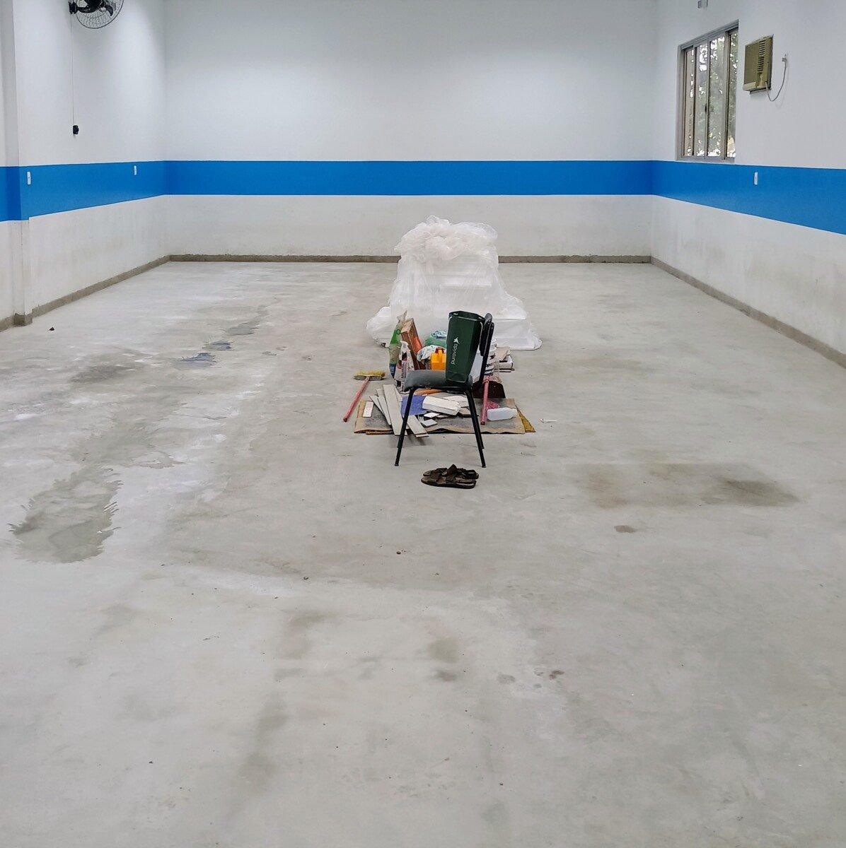 Antes: Sala ampla vazia, com piso de cimento e faixa azul na parede
