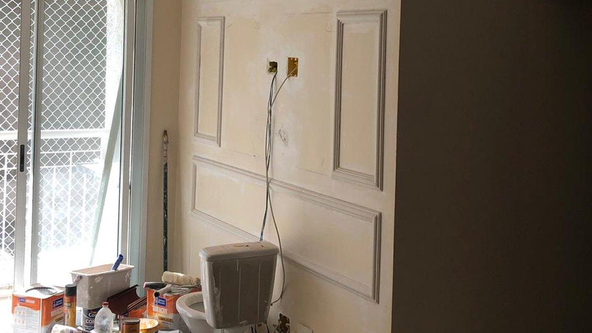 Antes: Parede da sala com molduras em obra, materiais e fios aparentes