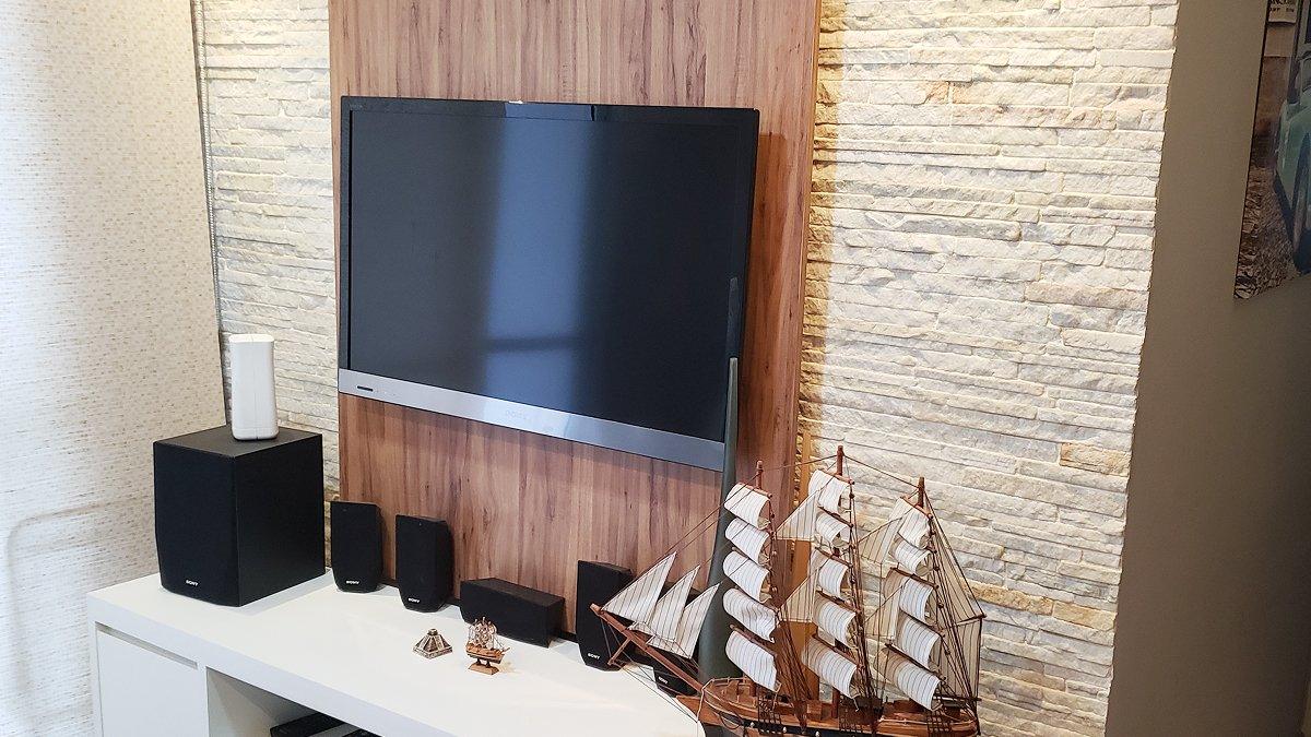 Depois: Sala pronta com rack branco, painel de pedra e televisão