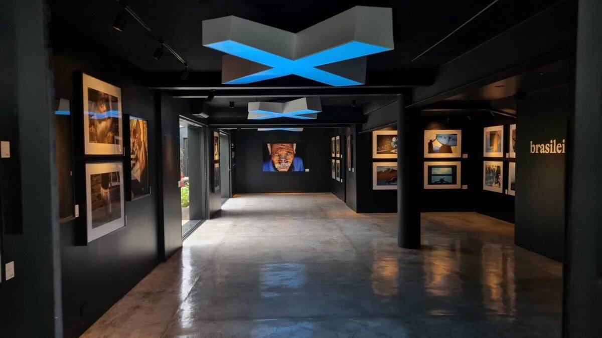 Depois: Galeria pronta com paredes pretas, fotos iluminadas e luminária em X no teto