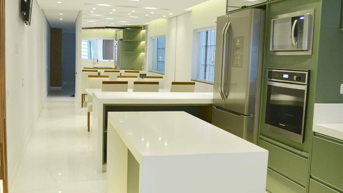 Depois: Cozinha integrada pronta, com ilha branca e armários verdes